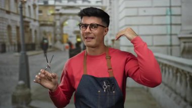 Şehrin caddesinde elinde makas tutan genç İspanyol adam gözlüklü önlüklü gülümsüyor. Dışarıdan kendine güvenen dış plan resmine benziyor..