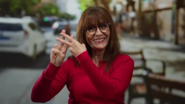 Kırmızı kazaklı İspanyol bir kadın işlek bir caddede hashtag sembolü yapıyor..