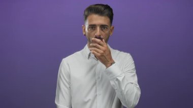 Adam elini mor stüdyoda temiz beyaz gömlek ve geniş bakışlı ifade giyerek ağzını kapatıyor..