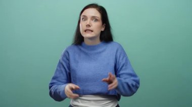 Mavi süveter giymiş, yeşil arka planda hareket eden ve elleri rahat bir şekilde vurgu yapan bir kadın..