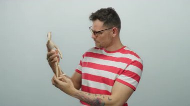 Gözlüklü genç adam beyaz arka planda çizgili gömlekli ahşap bir manken tutuyor. Odaklanma ve yaratıcılık gösteriyor..