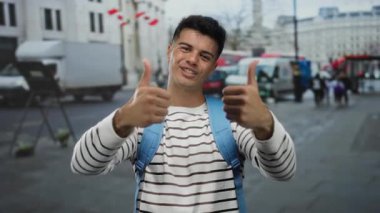 Çizgili gömlekli genç adam hareketli bir şehir caddesinde canlı ve modern şehir atmosferini yakalarken başparmağını kaldırıyor..