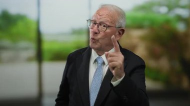 Takım elbiseli kıdemli bir adam düşünceli bir şekilde parkın içinde el kol hareketi yaparak iş odaklarının ve doğanın sükunetini yakalıyor..