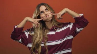 Çizgili gömlekli sarışın kadın fotoğraf stüdyosunda parmaklarıyla yanaklarını bastırır; neşe neşesi gençlik.