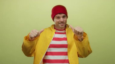 Sarı yağmurluklu ve kırmızı bereli İspanyol genç adam sarı arka planda kendini işaret ediyor. Kendine güveni ve kendine güveni var ve gülümsüyor..