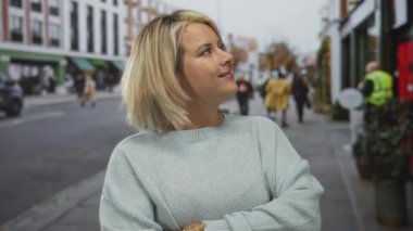 Gülümseyen genç sarışın kadın kalabalık şehir caddesinde ellerini açık tutuyor..
