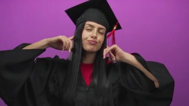 Şapkalı ve cüppeli genç İspanyol kadın kulaklarını parlak mor bir arka plan karşısında parmaklarıyla kapatıyor..