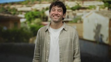 Büyüleyici bir Akdeniz kasabasında gülümseyen İspanyol bir adam, günlük kıyafetler giyiyor, geleneksel kırsal mimarinin ortasında sıcaklığı ve dostluğu taşıyor..