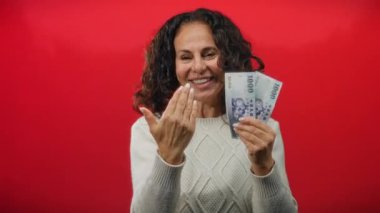 Tayvan banknotlarını canlı kırmızı bir arkaplanda sergileyen bir kadın, davetkar bir gülümsemeyle finansal fırsatlar sunuyor..