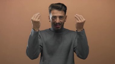 Adam stüdyoda şeftali arkaplanına karşı iki eliyle çimdiklenmiş italyan hareketi yapıyor. İletişim merakını sorguluyor..