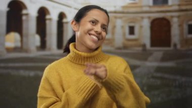 Sarı bir kazakla mutlu bir şekilde gülümseyen bir kadın. Arka planda kemerler olan eski bir kasabada, huzurlu bir anda neşe ifade ediyor..