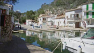 Mallorca 'daki Cala Figür Limanı' nın bulanık görüntüsü. Odaklanmış tekneler ve açık mavi gökyüzünün altında yürüyen insanlar..