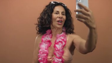 Mayolu İspanyol kadın ve Lei, izole olmuş kahverengi bir duvara selfie çekiyorlar. Orta yaşlı neşeli bir yaz havası sergiliyorlar..