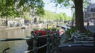 Bisikletler, bulanık teknelerle ve yemyeşil ağaçlarla dolu bir kanala bakan ve Hollanda şehir manzarasında rüya gibi bir atmosfer yaratan bir çit..