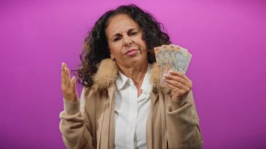 Romanyalı banknotları tutan orta yaşlı bir kadın canlı mor bir geçmişe karşı kafa karışıklığı göstererek, mali belirsizliği öne sürüyor.