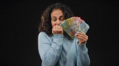 Orta yaşlı bir kadın Avustralya banknotlarını gergin bir şekilde siyah bir arkaplanda tutuyor..