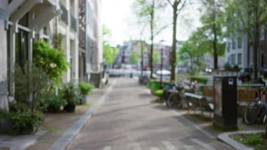 Bisiklet ve ağaçlarla dağılmış bir kentsel caddenin yer aldığı Avrupa şehir manzarası, berrak gökyüzü altında bulanık binalar ve patikalarla sakin bir açık hava manzarası yakalıyor.