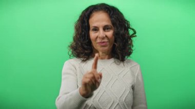 Yeşil arka planda kameraya doğru kıvırcık saçlı, rahat bir süveter giyen olgun bir kadın..