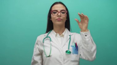 Yeşil bir duvarın önünde gözlük ve steteskop takan İspanyol doktor tıp üniformasıyla mutluluğu ifade ediyor..