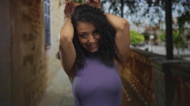 Hispanik kadın taş korkulukların yanında baş üzerinde elleri ile kulak hareketi yapıyor; oyuncu bir an.