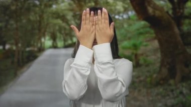 Serin bir parkta ellerini kaldırmış neşeyle gülümseyen bir kadın, açık havada gençlik enerjisi ve mutluluk sergiliyor..