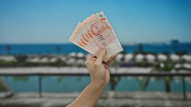 Güneşli bir sahilde el ele tutuşan paralar, rahat ve manzaralı bir ortamda sergilenen para, seyahat ve finansal temalar için mükemmel..