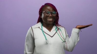 Afro-Amerikalı bir kadın gülümseyip boynunda steteskopla açık elini işaret ederek izole edilmiş mor bir arka plan duvarının üzerinden sunum ya da tanıtım kavramını aktarıyor..
