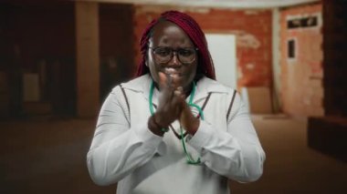 Kadın inşaat alanında elini ovuşturarak soğuk havanın gözlük ve steteskop taktığını söylüyor..