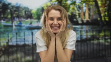 Parkta güneşli bir günün tadını çıkaran bir kadın. Etrafı mutlu bir ifadeyle çevrili ve elleri yüzünde, neşe ve şaşkınlık dolu bir ifadeyle.