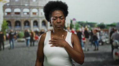 Roma Kolezyumu 'nun yanında duran kadın, gündüz vakti Roma' da tarihi turizm sergileyen beyaz bluz giymiş, eli göğsünde yorgun görünüyor..