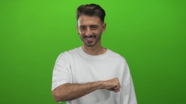 Erkek, canlı yeşil bir stüdyo duvarına karşı başparmağıyla kolunu kaldırır. Pozitiflik..