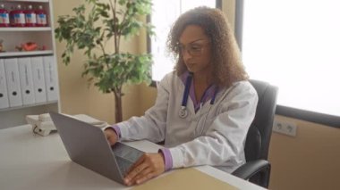 Steteskop takan kadın doktor masada oturur ve dizüstü bilgisayarda yazar ve bina içinde boyuna dokunur; stres.