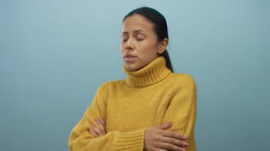 Sarı kazak giyen bir kadın, düşünceli bir ifadeyle koyu mavi bir arkaplan karşısında izole bir şekilde duruyor. Bu da bir stüdyo ortamında iç gözlem ya da tefekkür olduğunu gösteriyor..