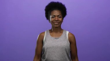 Kadın, güven ve ifadeyi vurgulayan münferit mor arka plana gülümserken kaya hareketi yapıyor.