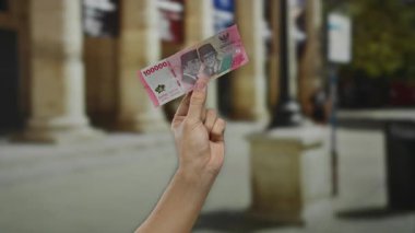 Bir Endonezya rupiah banknotunu şehir sokaklarında elinde tutan bir adamın eli..