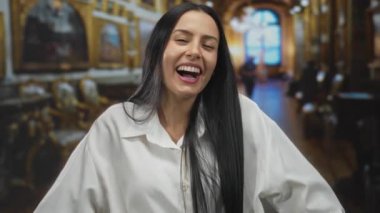 Müzede uzun saçlı genç bir kadın zarif bir salon ortamında karışık duygular ifade ediyor. Üzüntüden mutluluğa geçişi sergiliyor..