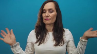 Mavi arka planda uzun saçları olan, gözleri kapalı, elleri havada, beyaz gömlekli, çeşitli duyguları ifade eden bir kadın.