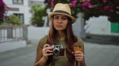 Dışarıdaki sokakta elinde kamera ve dondurma tutan bir kadın şapka takıyor, güneşli bir günde şehir sahnesinde gençlik yolculuğunu somutlaştırıyor..