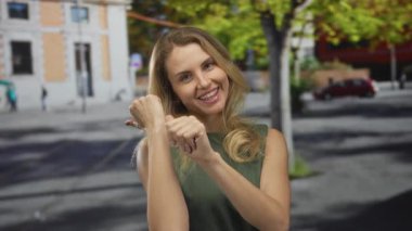 Yeşil elbiseli, kentsel sokak ortamında gülümseyen bir kadın güneşli bir şehir arka planında neşeli ve neşeli davranışlar sergiliyor..