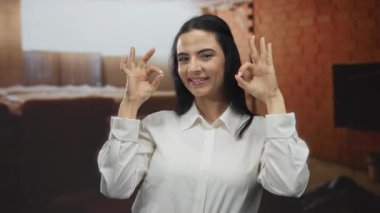 Beyaz tişörtlü genç İspanyol kadın, kırmızı tuğla duvarlarla çevrili kapalı bir inşaat alanında kendine güveni ve pozitifliği olan bir jest yapıyor..