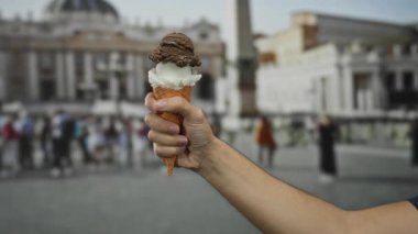 St. Peter Meydanı, Vatikan 'da elinde dondurma külahı tutan bir adam. Arka planda bulanık bir mimari, turistlerle şehir dışı manzarası sergiliyor..