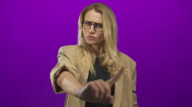 Kadın, parmak takan, gözlüklü ve spor ceketli ciddi yüz ifadesini vurgulayarak dramatik bir etki yaratmak için stüdyo ortamında izole edilmiş bir şekilde 