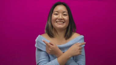 Genç bir kadın gülümsüyor ve pembe arka planda mavi kazak giyiyor neşeli duygular ve ifadeler aktarıyor.