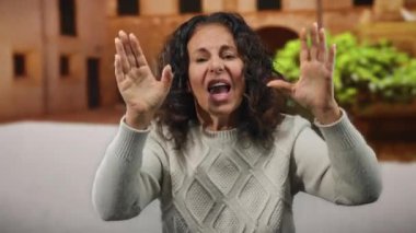 Şehirli bir sokakta, kıvırcık saçlı, örgü ören, hareketli ve canlı bir çevrede duygularını ifade eden bir kadın..