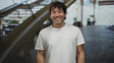 Havaalanında elleri sımsıkı kapalı gülümseyen İspanyol bir adam, seyahat sırasında neşesini ve dostluğunu ifade ediyor..