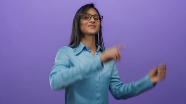 Mavi tişörtlü genç Latin kadın izole bir mor duvara yaslanıyor, canlı ve çekici bir neşe ve coşku ifadesi sergiliyor..