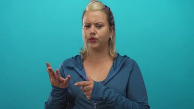 Stüdyoda mavi ceketli sarışın kadın parmaklarını odaklanmış ifadeyle ve çatık kaşlı kaşlarıyla sayıyor; belirsizlik..