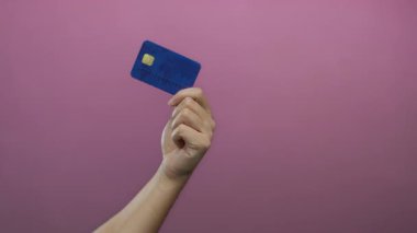 Kafkasyalı bir adamın elinde pembe bir duvara karşı mavi bir kredi kartı tutarken, canlı bir arka planda izole edilmiş, finans ve kişisel kredi kullanımını vurgulayan.