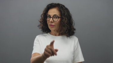 Gözlüklü ve beyaz tişörtlü İspanyol bir kadın, gri izole edilmiş arka plana güvenle işaret ediyor..