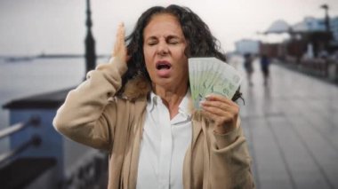 Singapur 'da, deniz kenarında orta yaşlı bir kadın, kalabalık bir liman bölgesinin yakınındaki gürültüden rahatsız olduğunu belirten bir ifadeyle, elinde Singapur doları tutuyordu..